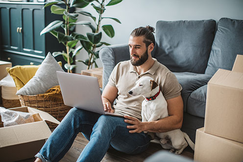 man sitting on the floor next to sofa with his dog using laptop